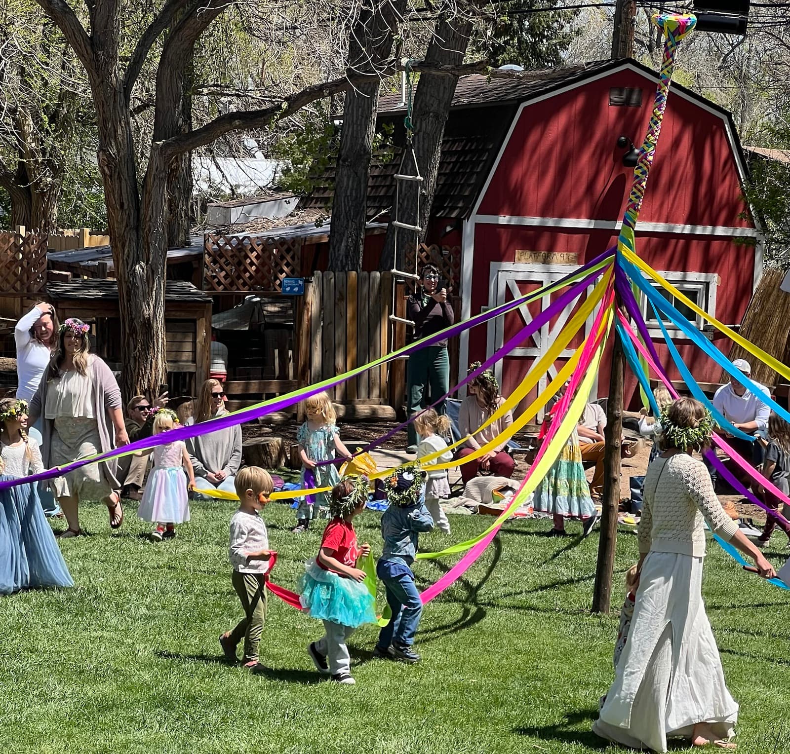 Children in flower crowns dancing round the maypole, ribbons in every color