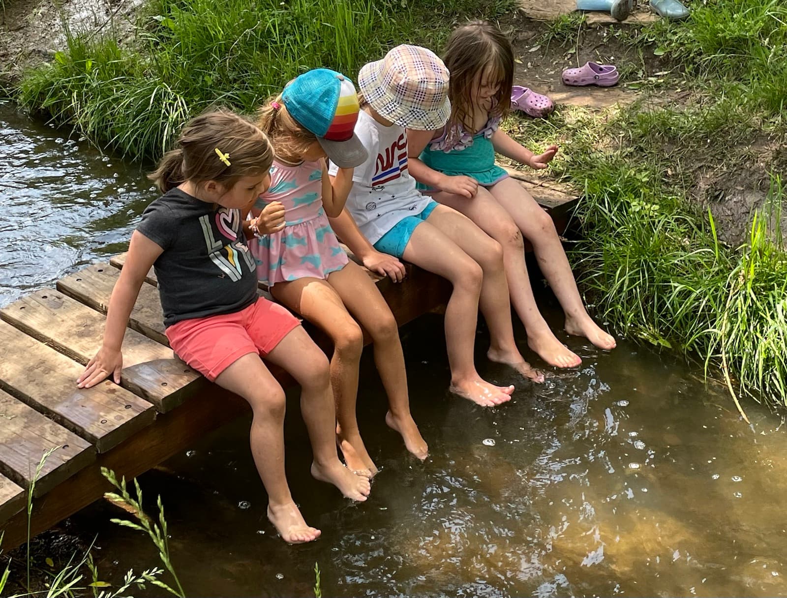 Four children on the footbridge, bare toes dangling in the creek