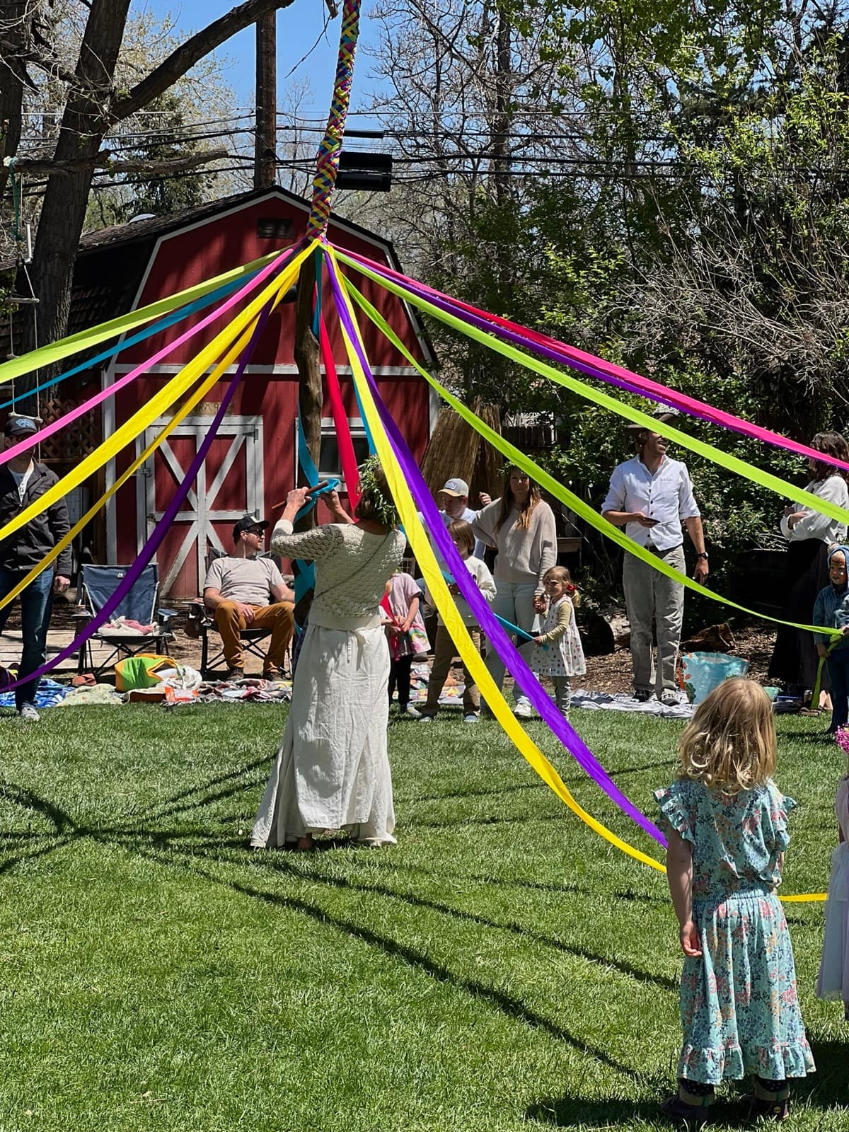 A grown-up and a child dancing round the maypole, ribbons streaming from the top of the pole