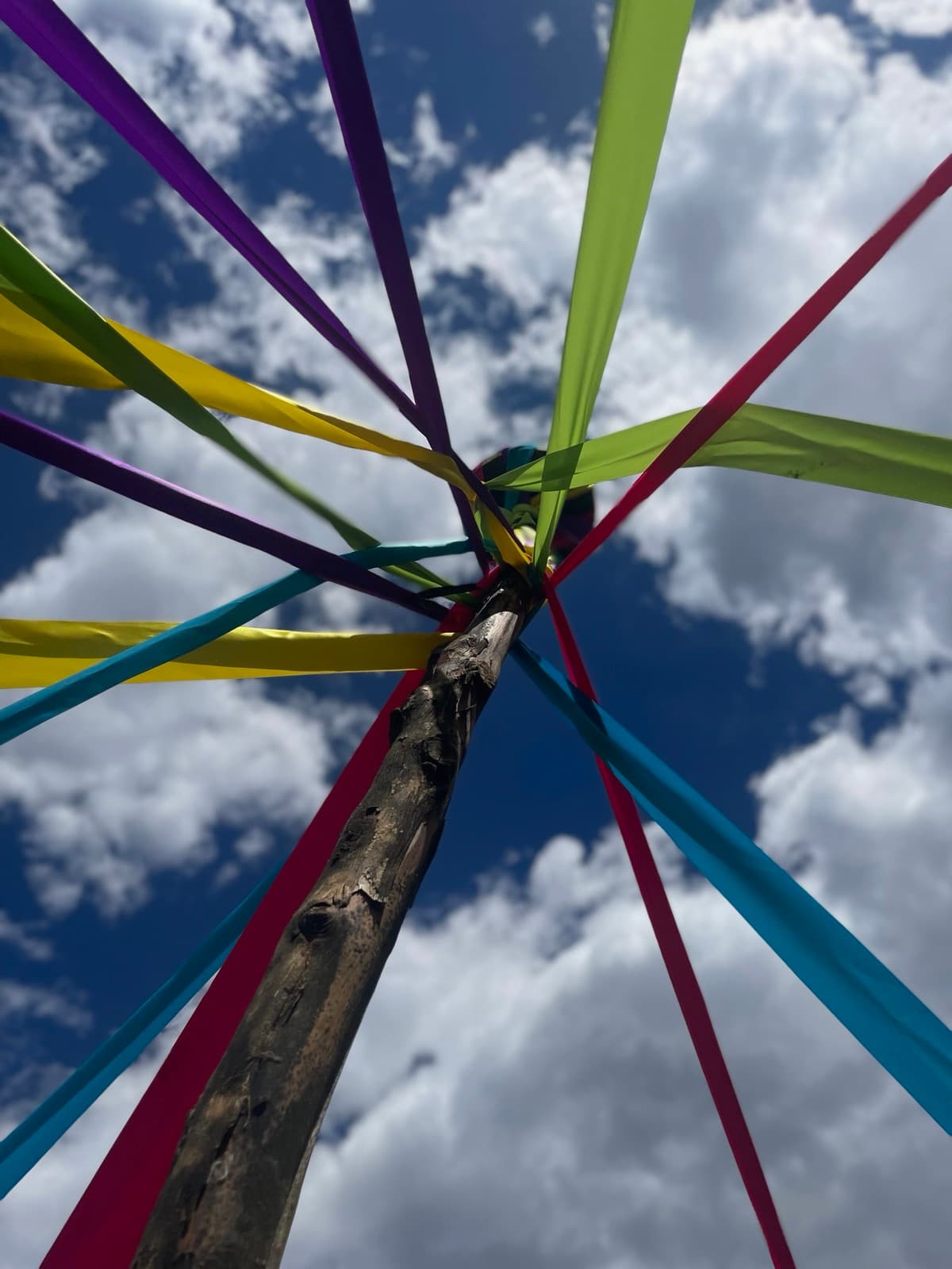 Maypole ribbons in every color fanning out against a blue sky, seen from below